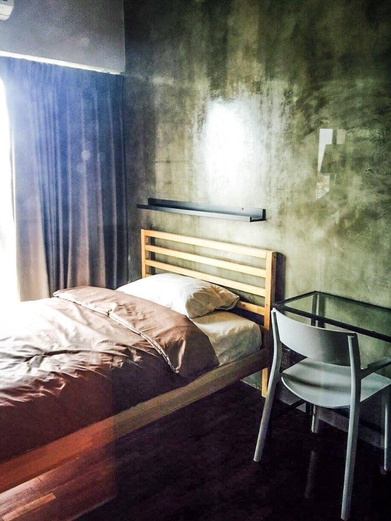 Loft-style studio room with exposed concrete walls, single bed, and study desk