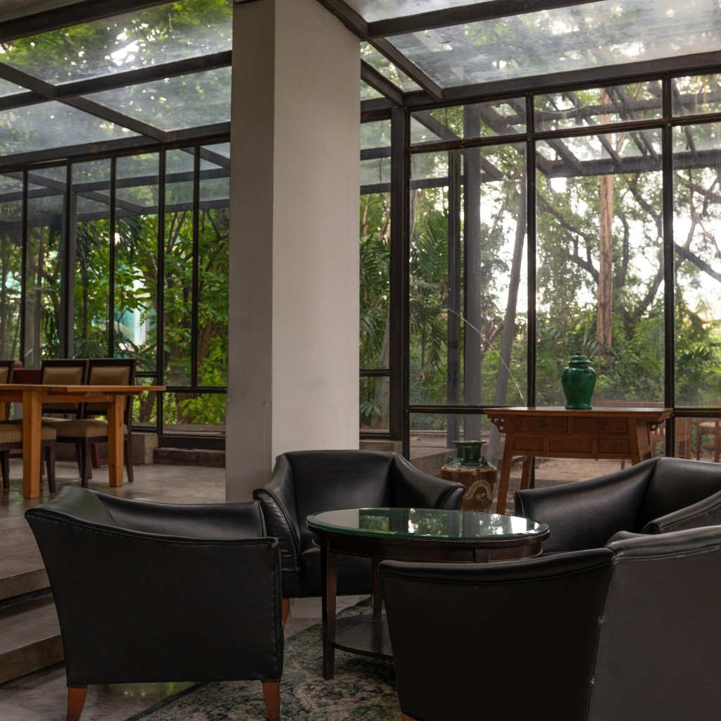 Glass-walled lounge with leather armchairs surrounded by greenery
